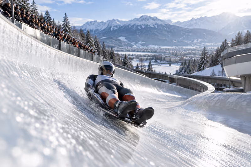 Spitzensportler auf einer eisigen Rodelbahn in einer verschneiten Tiroler Berglandschaft.