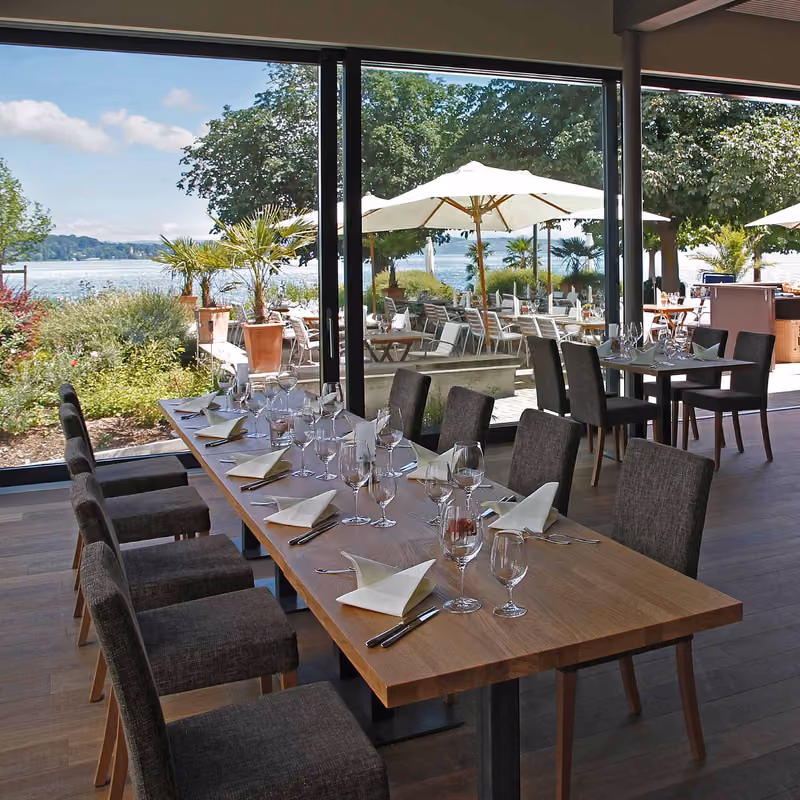 Gedeckte Tische im Fischerhaus mit Blick durch die Fenster auf Terrasse und Bodensee