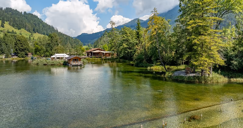 Forellensee mit Veranstaltungsbereichen am Ufer und Bergen im Hintergrund